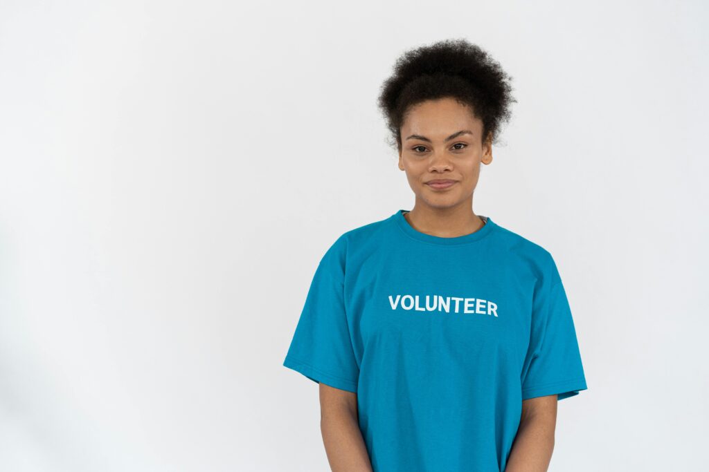 Smiling young woman in blue 'VOLUNTEER' t-shirt on white background.